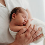 Gorgeous newborn in her fathers arms on a photoshoot in Cheshire