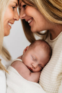 new parents laughing as they hold their sleeping newborn baby