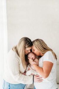 Two new mothers kissing their baby on a newborn photoshoot near Wilmslow