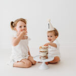 Baby boy eating cake on natural cake smash in Cheshire with sister