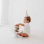 Baby boy eating cake on natural cake smash in Cheshire laughing