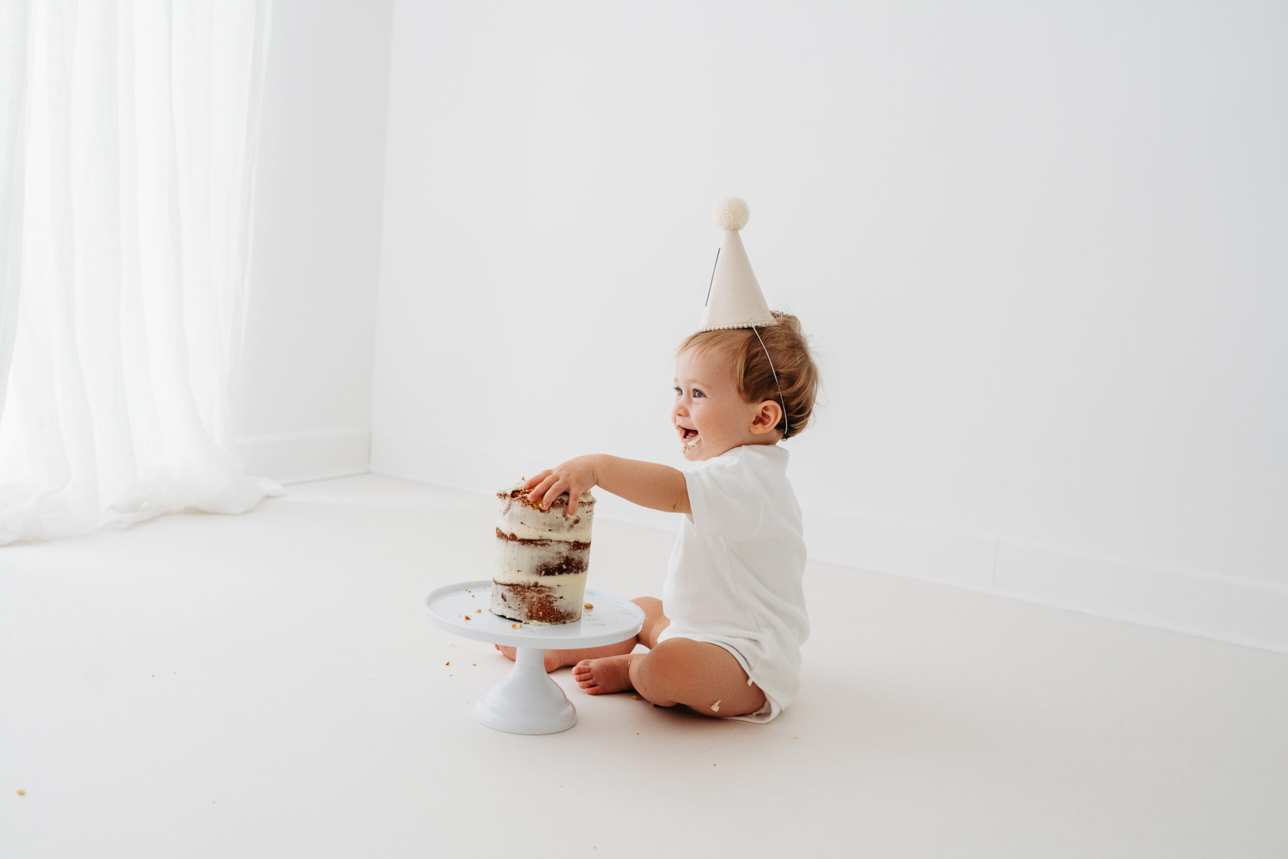 Baby boy eating cake on natural cake smash in Cheshire laughing