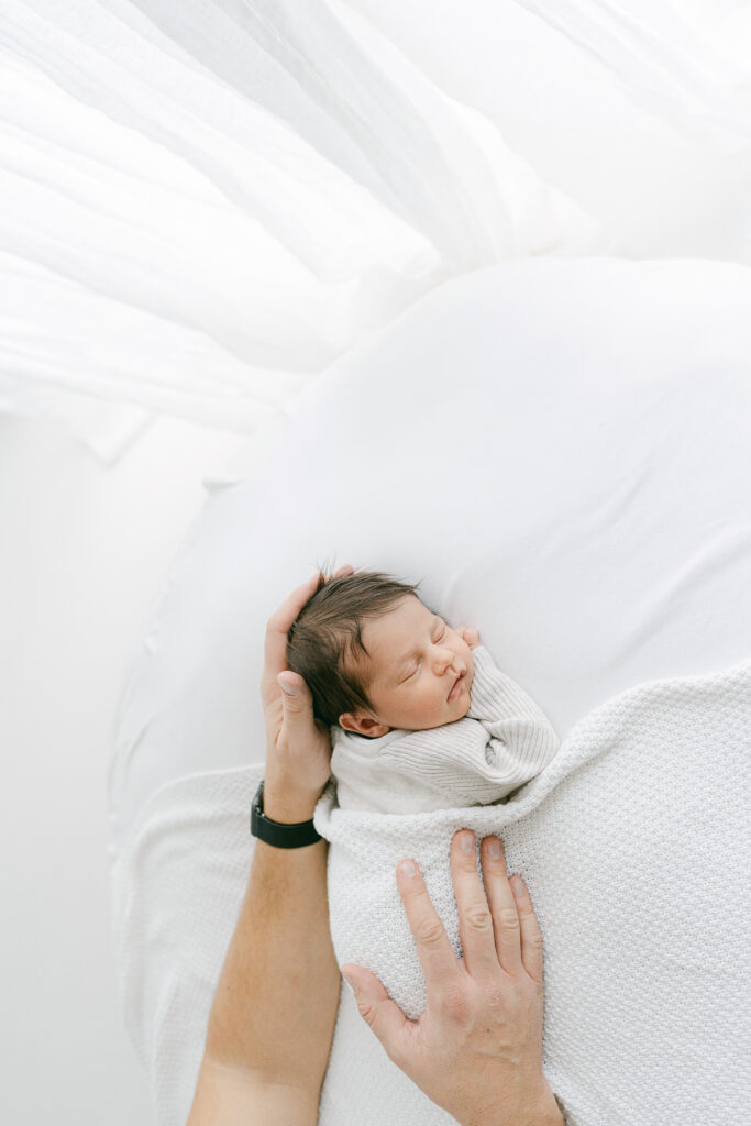 Fathers hands gently resting on sleeping newborn