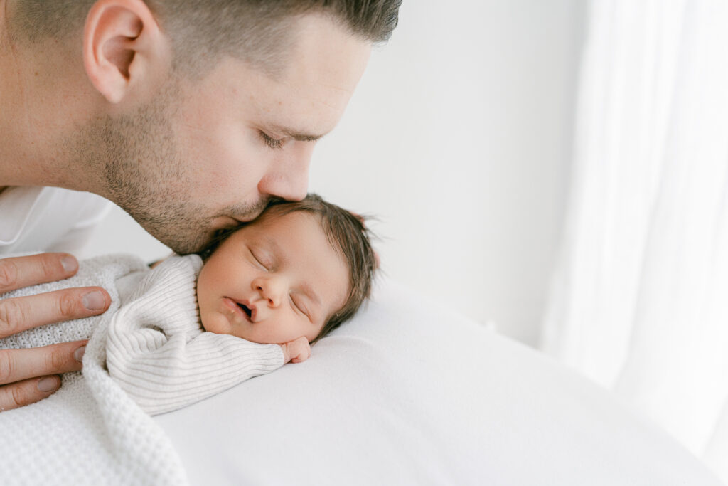 Father kissing newborn gently on cheek during a photoshoot