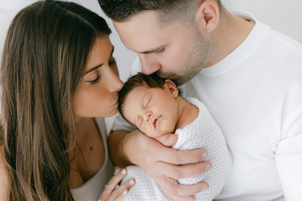 New parents kissing their newborn baby girl on a photoshoot in Cheshire