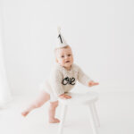 Baby boy in gorgeous ONE birthday jumper standing up on his cake smash photoshoot in Cheshire