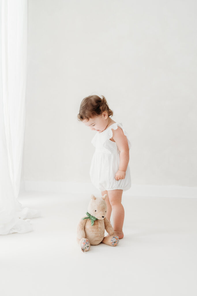 Little girl sitting on a stool looking at her teddy on her toddler photoshoot in Cheshire