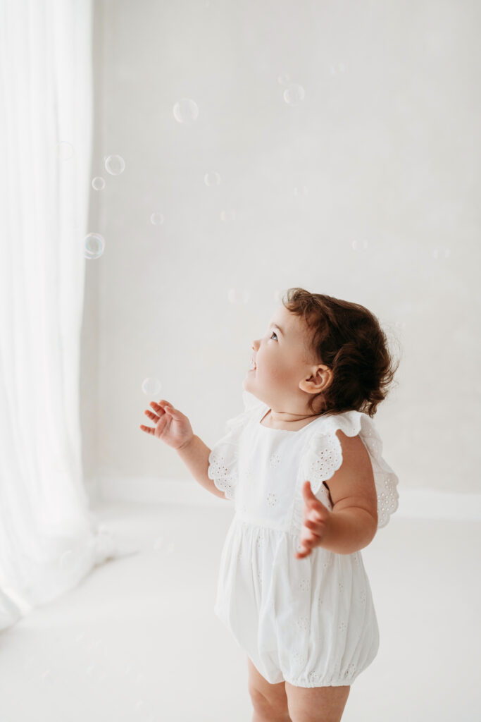 Young toddler looking up at bubbles on her natural toddler photoshoot in Cheshire